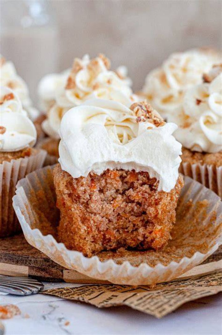 Carrot cake cupcake topped with swirled brown sugar frosting on a grey plate next to a fork.
