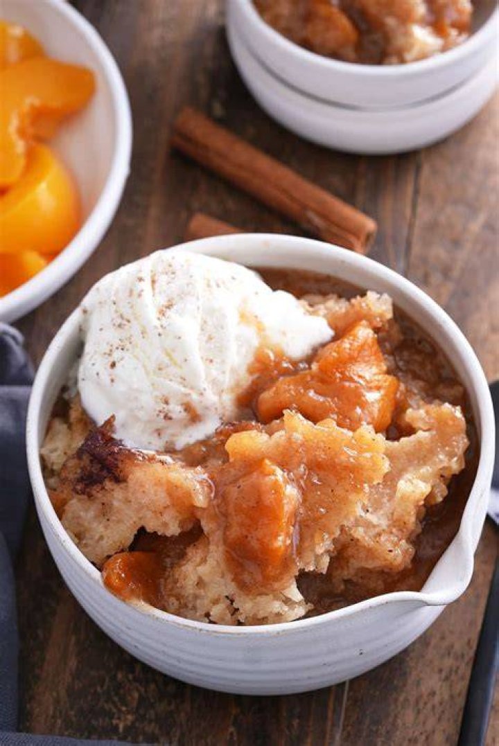 Peach Cobbler in a white bowl topped with a scoop of vanilla ice cream.